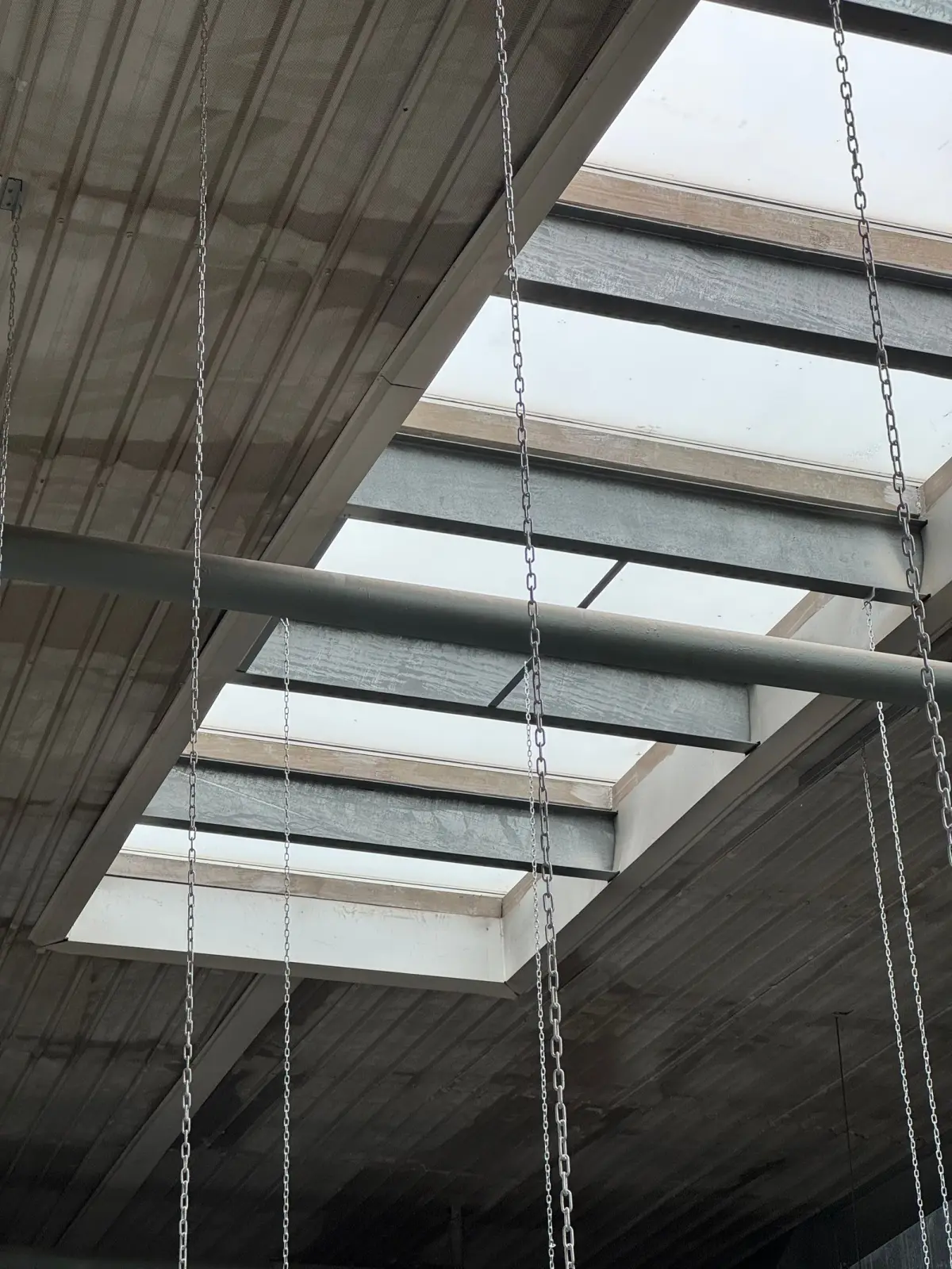 Stalen liggers onder een betonnen dak, met daglicht door een lichtstraat.
